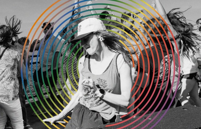 A group of people dancing energetically outdoors. The image is overlaid with colorful concentric circles creating a dynamic effect.