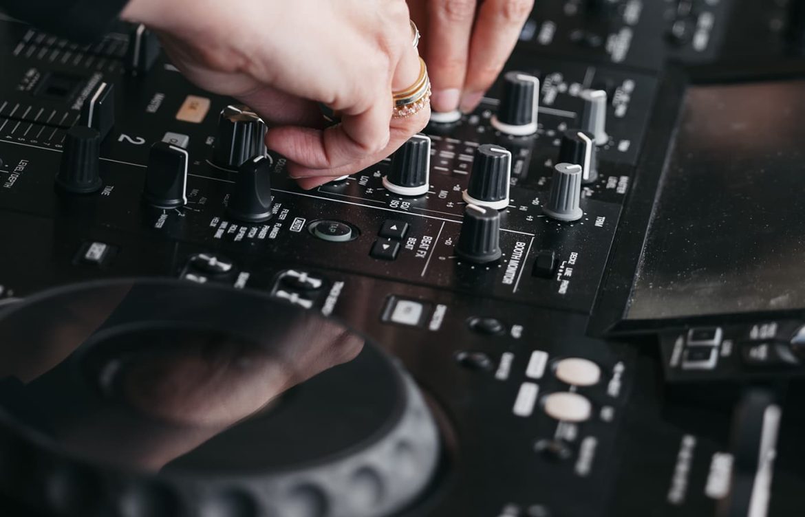 Hands adjusting knobs on a professional DJ mixer, featuring equipment from Pioneer.